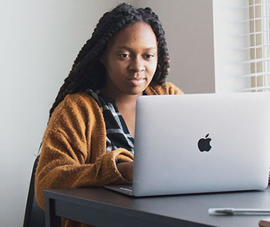 Black female student using Macbook on table